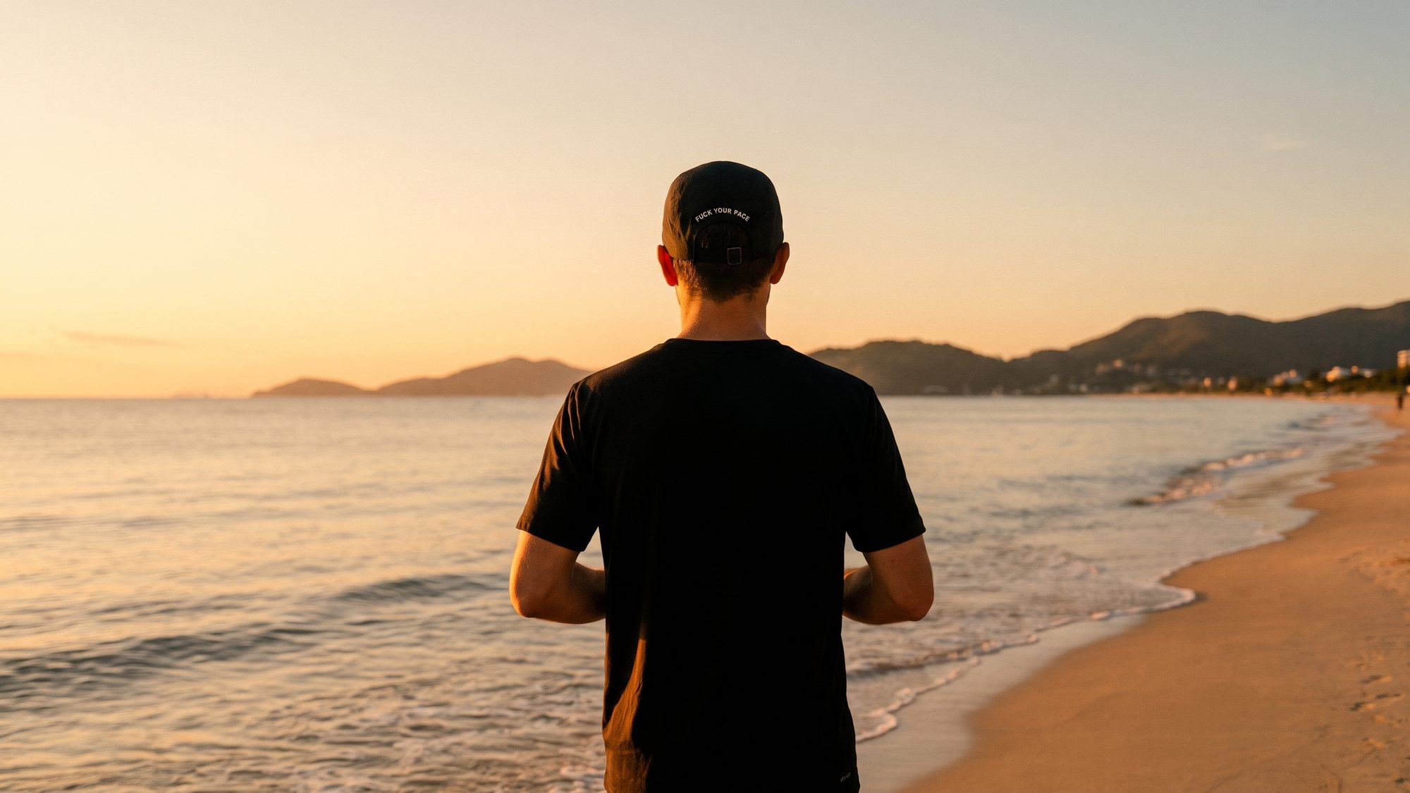 Corredor de costas na beira da praia ao nascer do sol, com o boné UNPACED